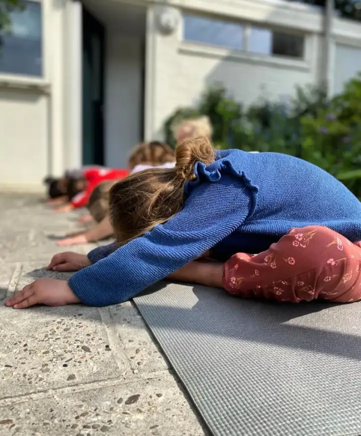 Kinderen doen samen ontspanningsoefeningen op matjes buiten
