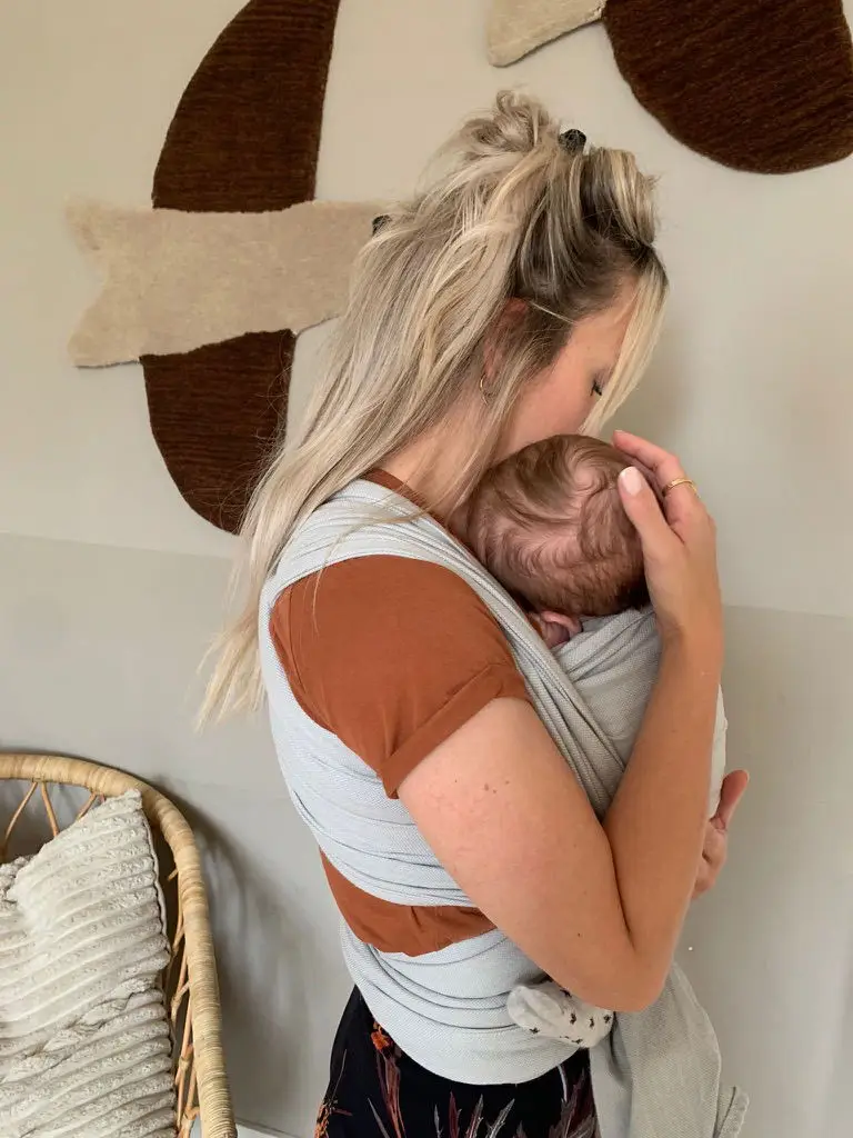 Pedagogisch medewerker houdt een baby geborgen vast in een draagdoek