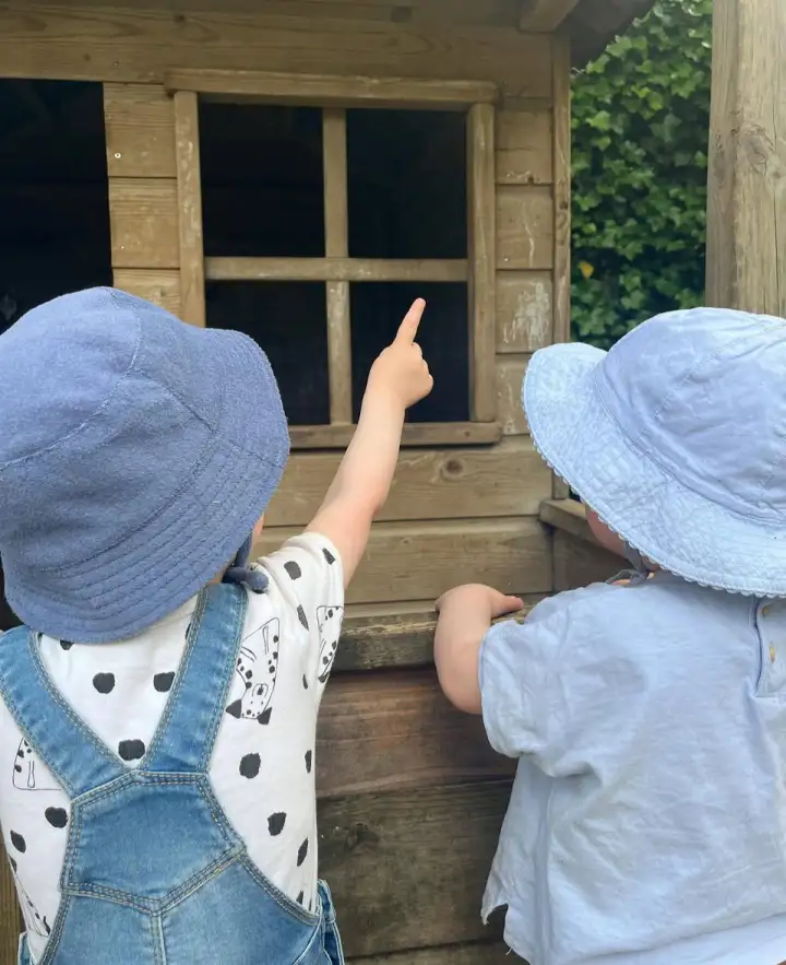 Twee peuters kijken samen bij het speelhuisje